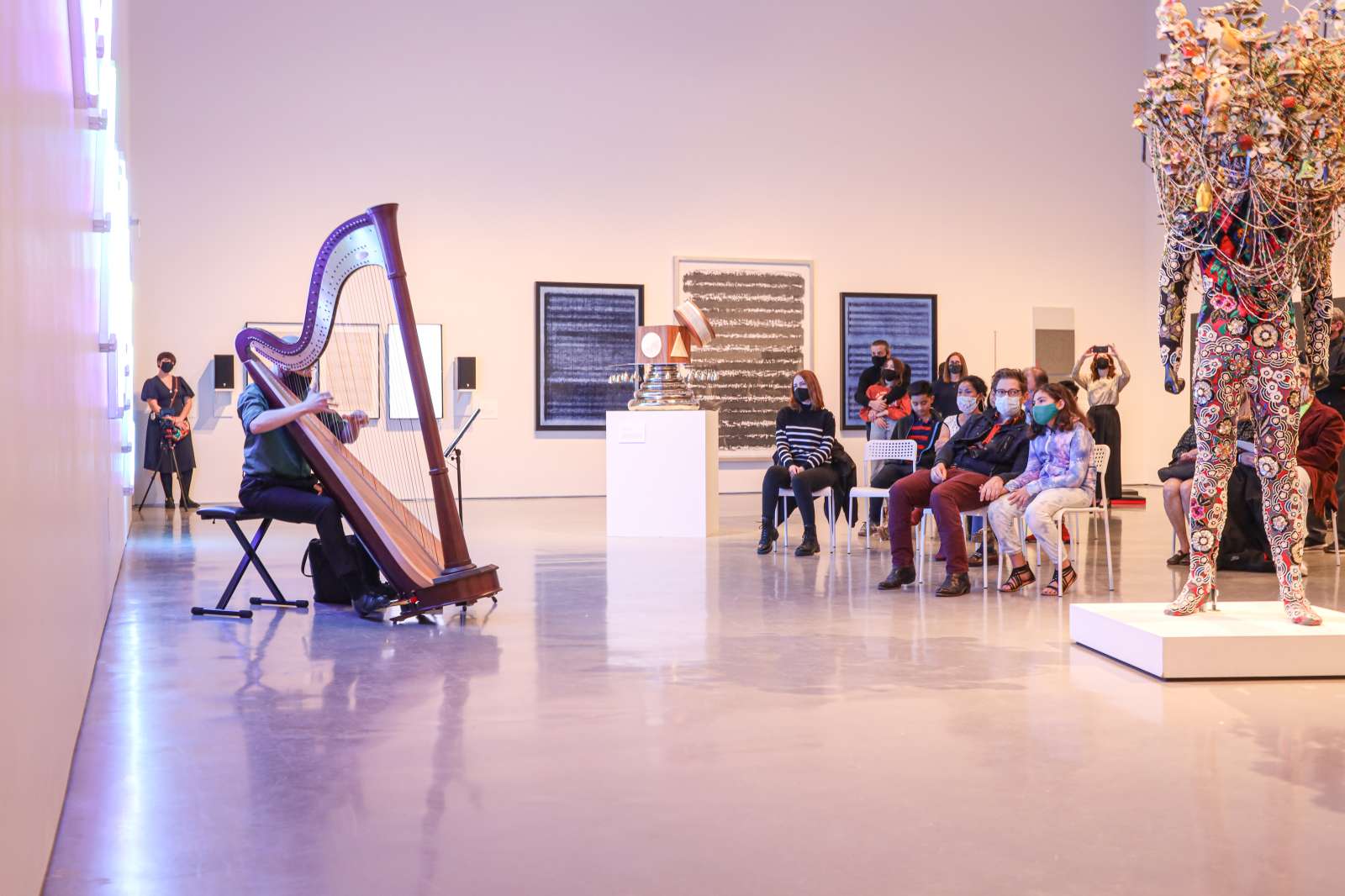 Harpist Performing on the left side of the screen to an audience pictured on the right side.