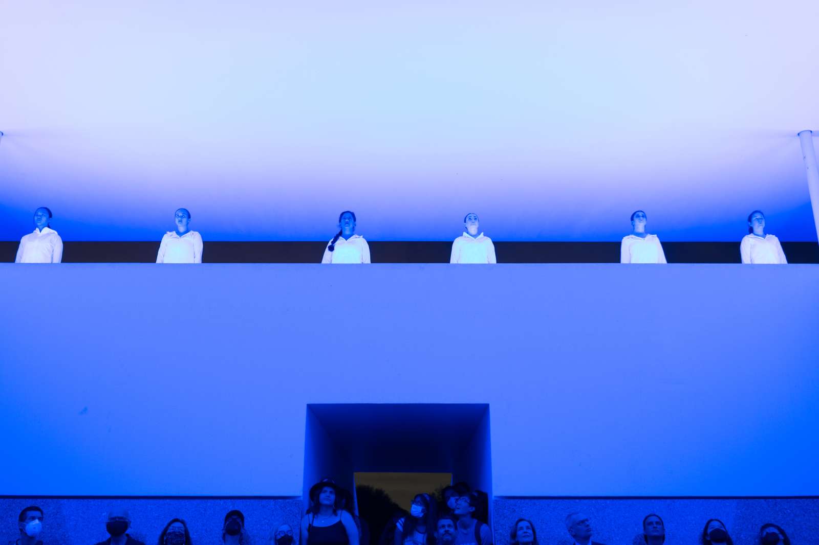 Six dancers illuminated by blue light while performing above audience