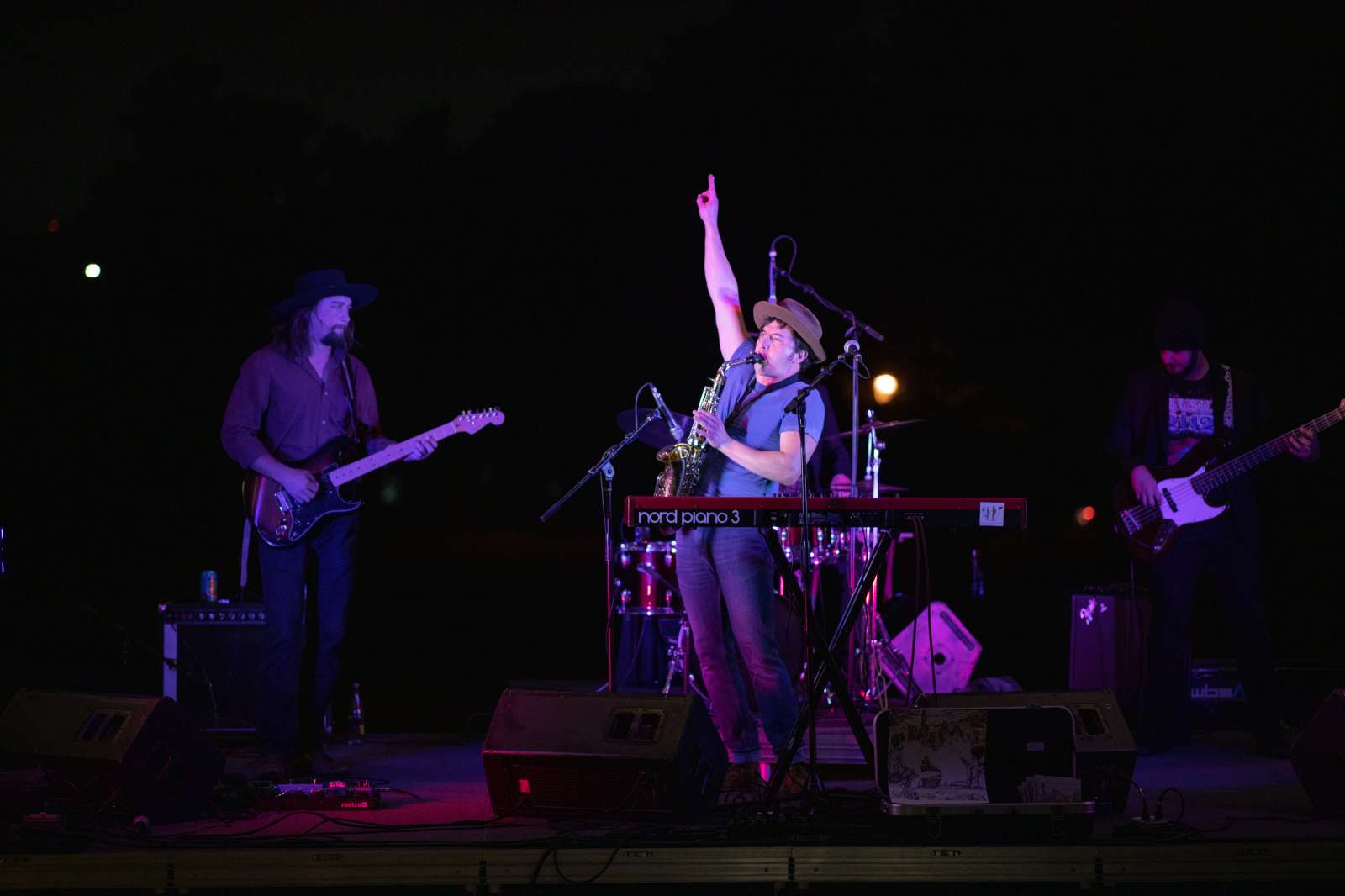 Man wearing a hat plays the saxophone while standing and pointing into the air