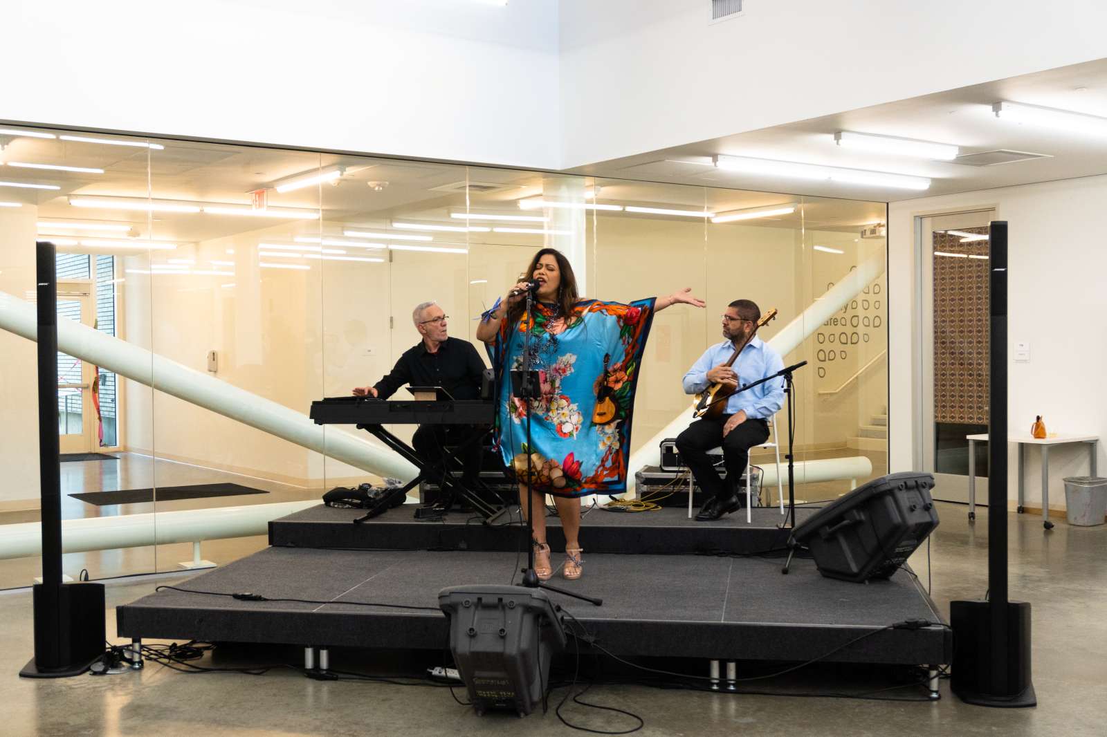 Performer wearing a blue and orange dress sings on a black raised platform