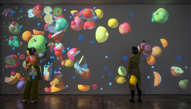 Women moving projected images of fruit around the wall with a VR controller